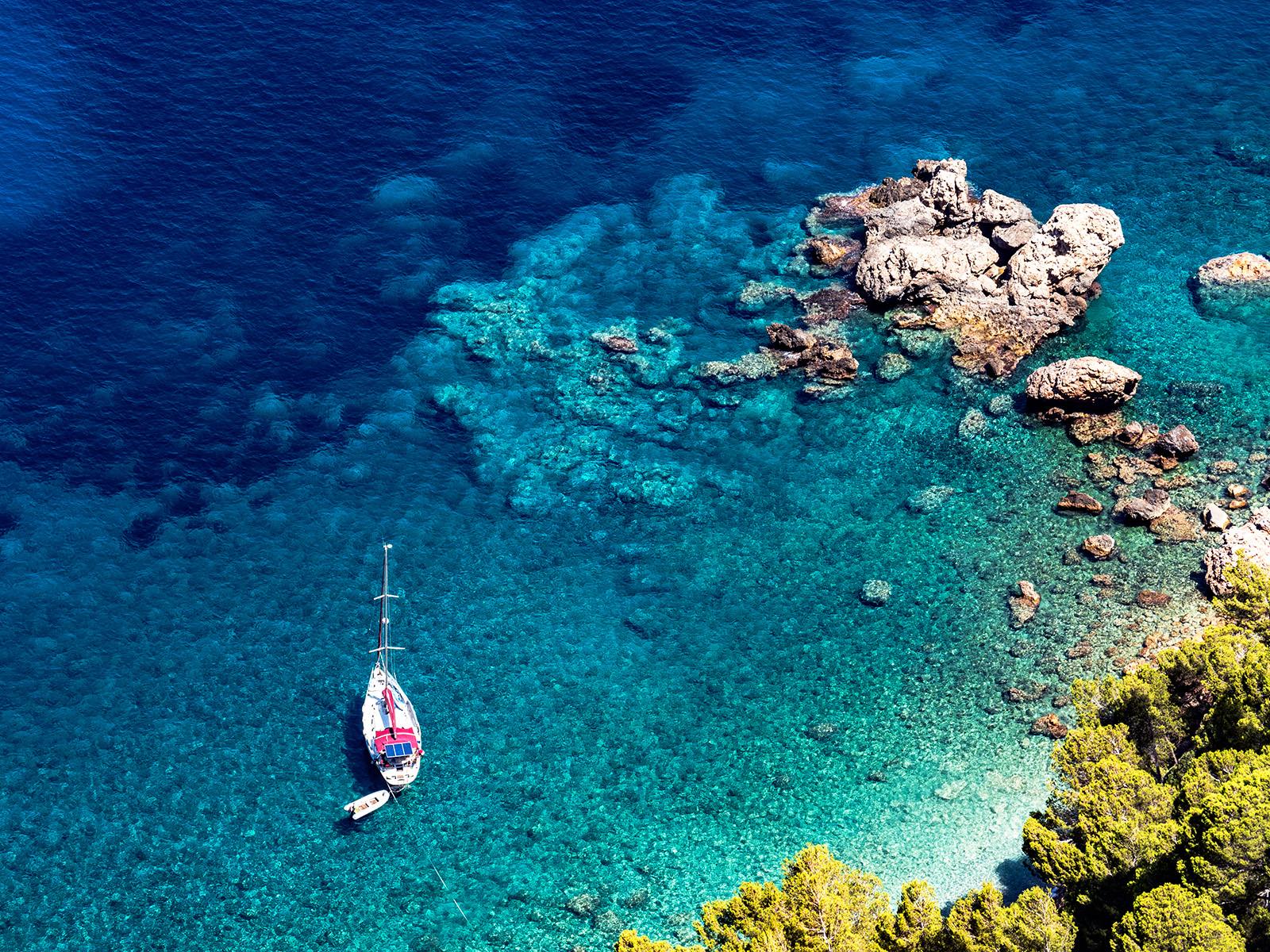 Bird's eye shot of rocky beach, small boat, blue water.