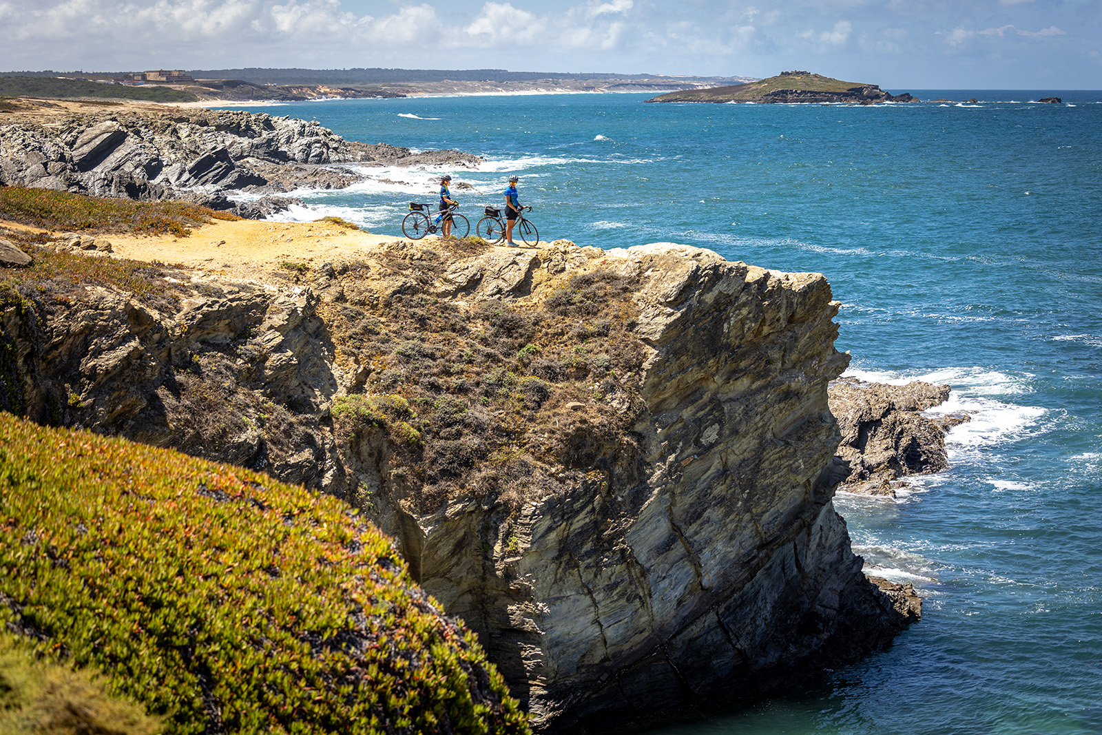 Two bikers resting on a cliff overlooking the sea