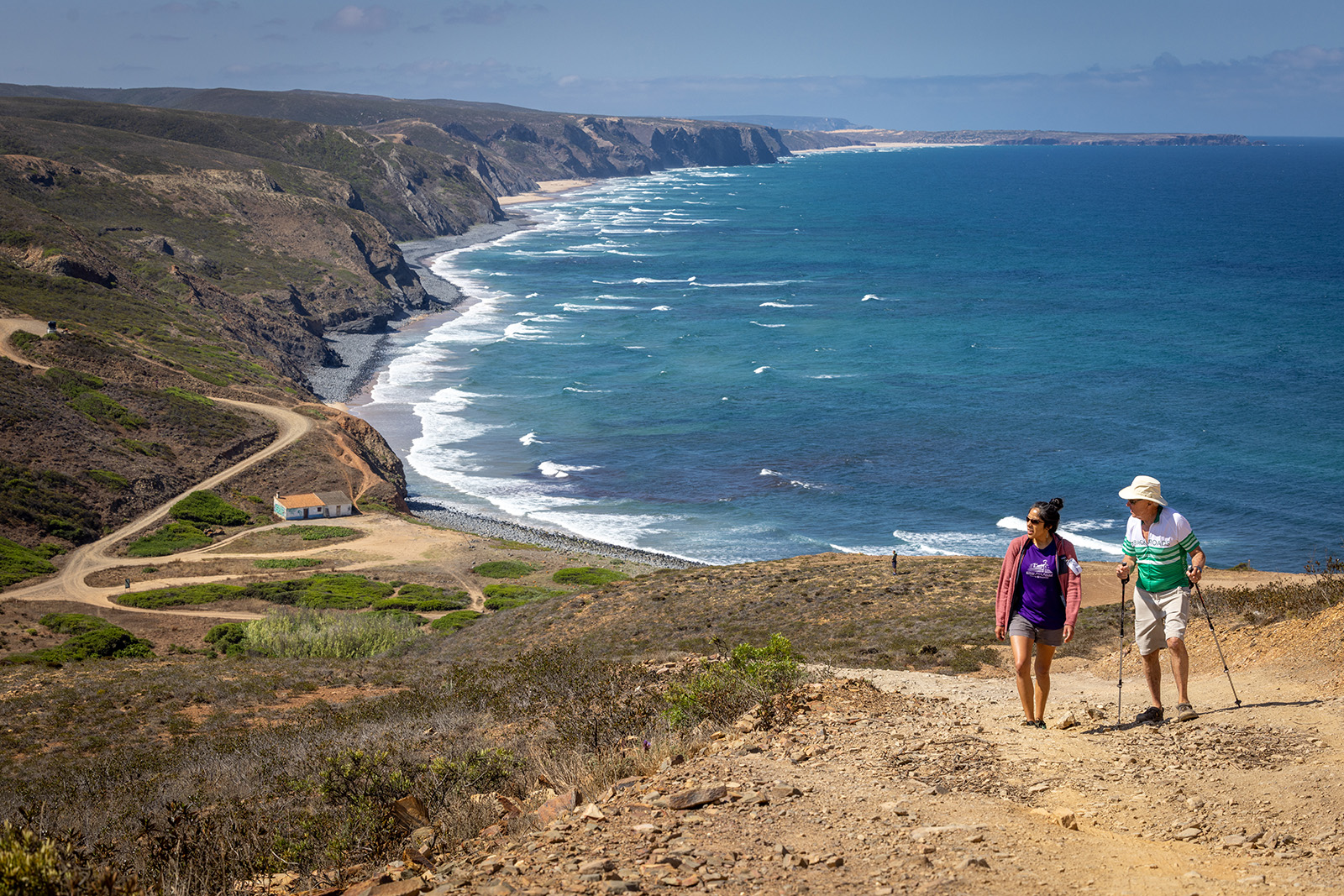 Two hikers walking up a sandy hill with the ocean in the background