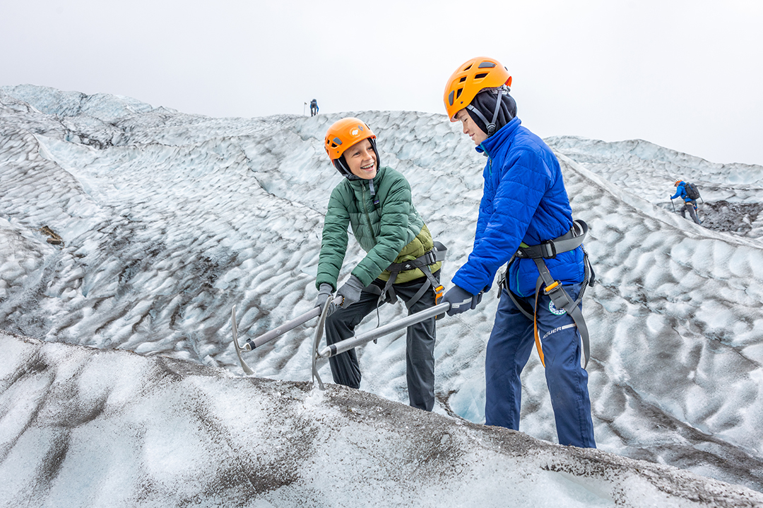 Two boys wearing safety helmets, using pickaxes to break snow