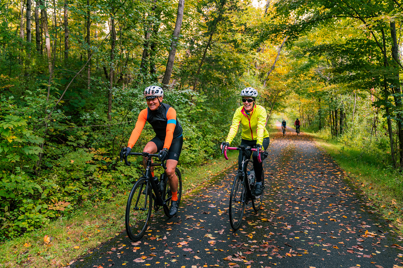 Two bikers biking down a tree lined road
