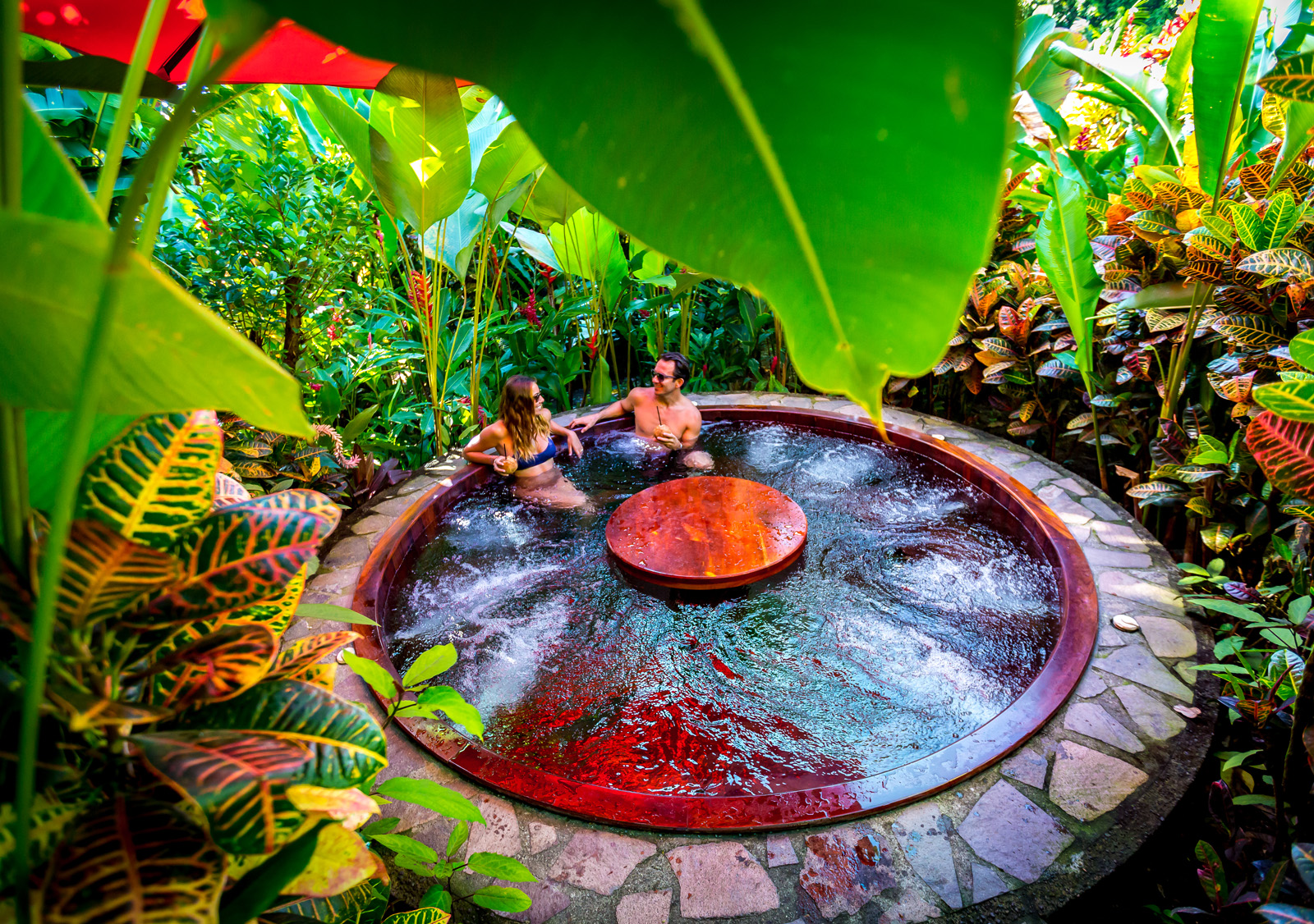 Man and woman in a red hot tub with a table in the center