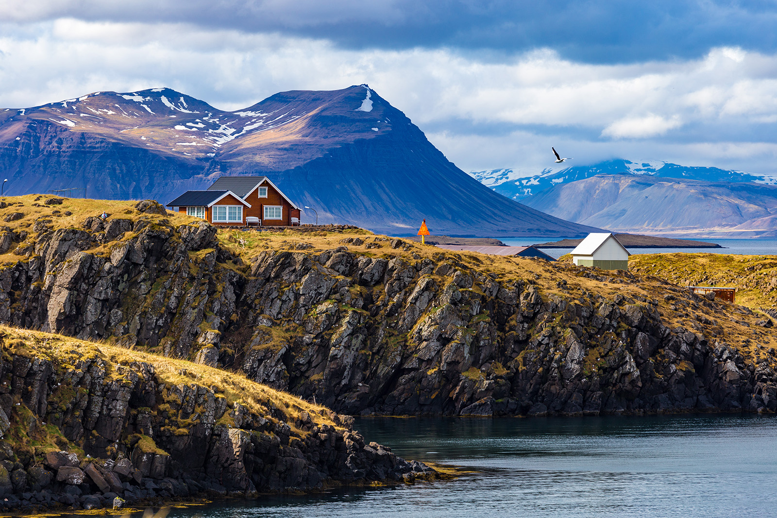 Red buildings on top of a jagged cliff next to the ocean