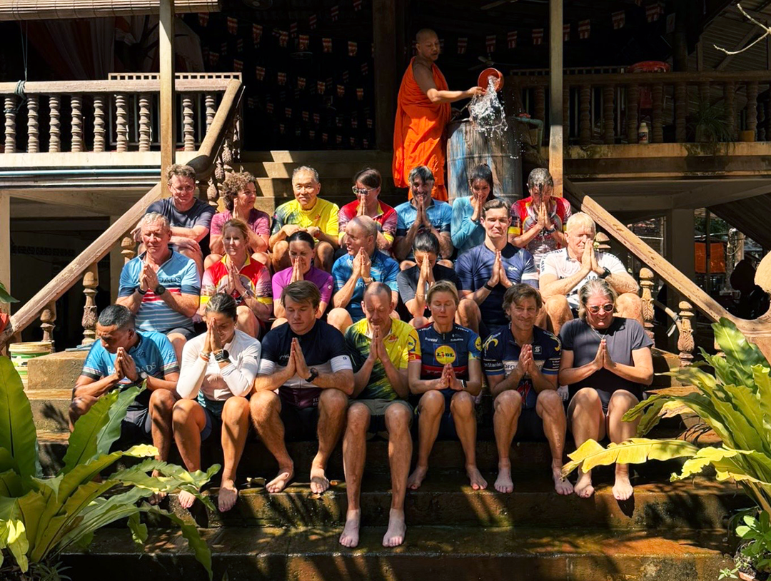 Group of people sitting on a flight of stairs, with a monk on top throwing water on them