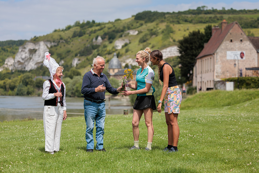 Three women and on man standing in a grass field, holding a small bouquet of flowers