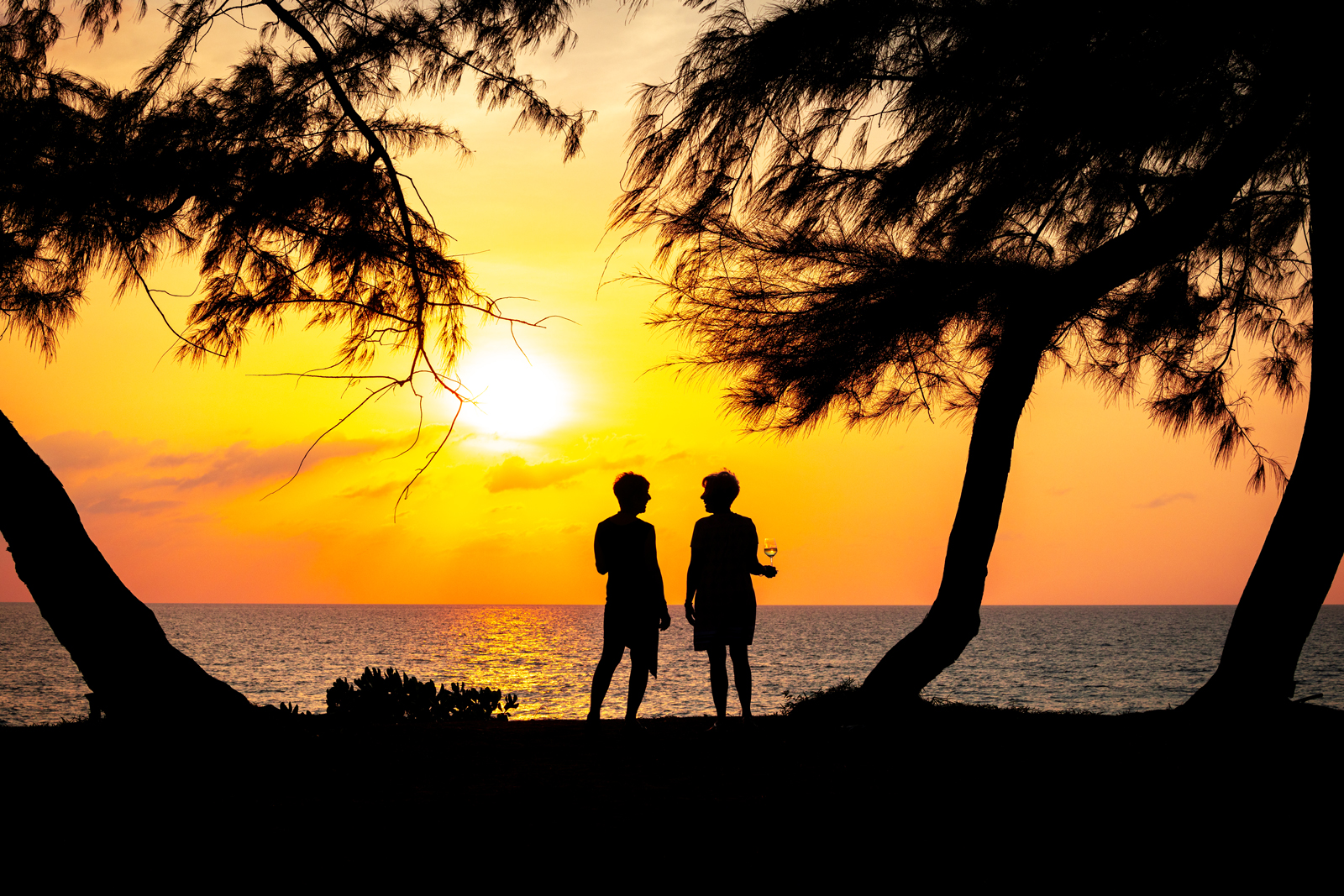 Silhouette of two people standing in front of a beach with the ocean and sunset in front