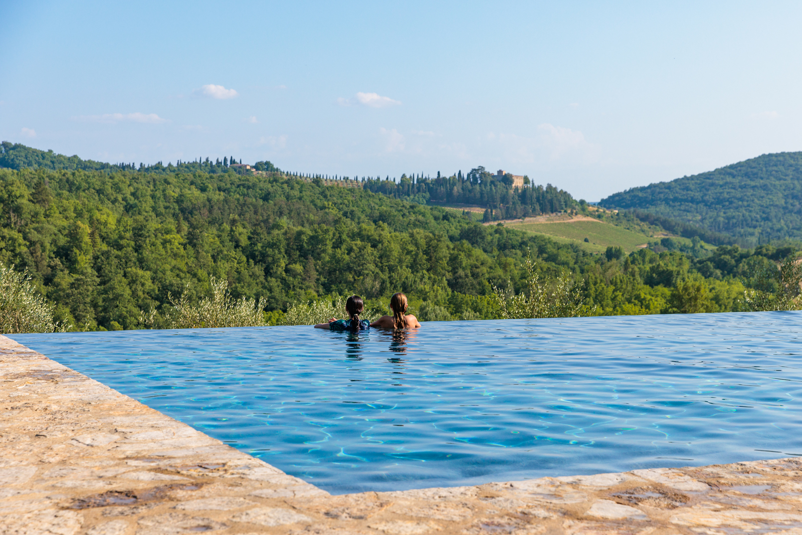 Two people in a pool, looking out to a large forest