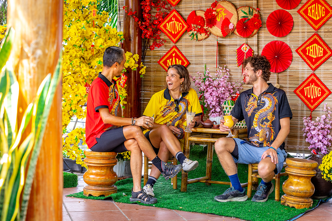 Two men and one woman sitting on wooden chairs in front of Vietnamese art pieces