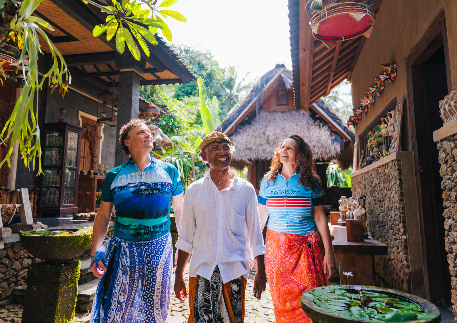 Two men and one woman smiling while walking through an alleyway of houses