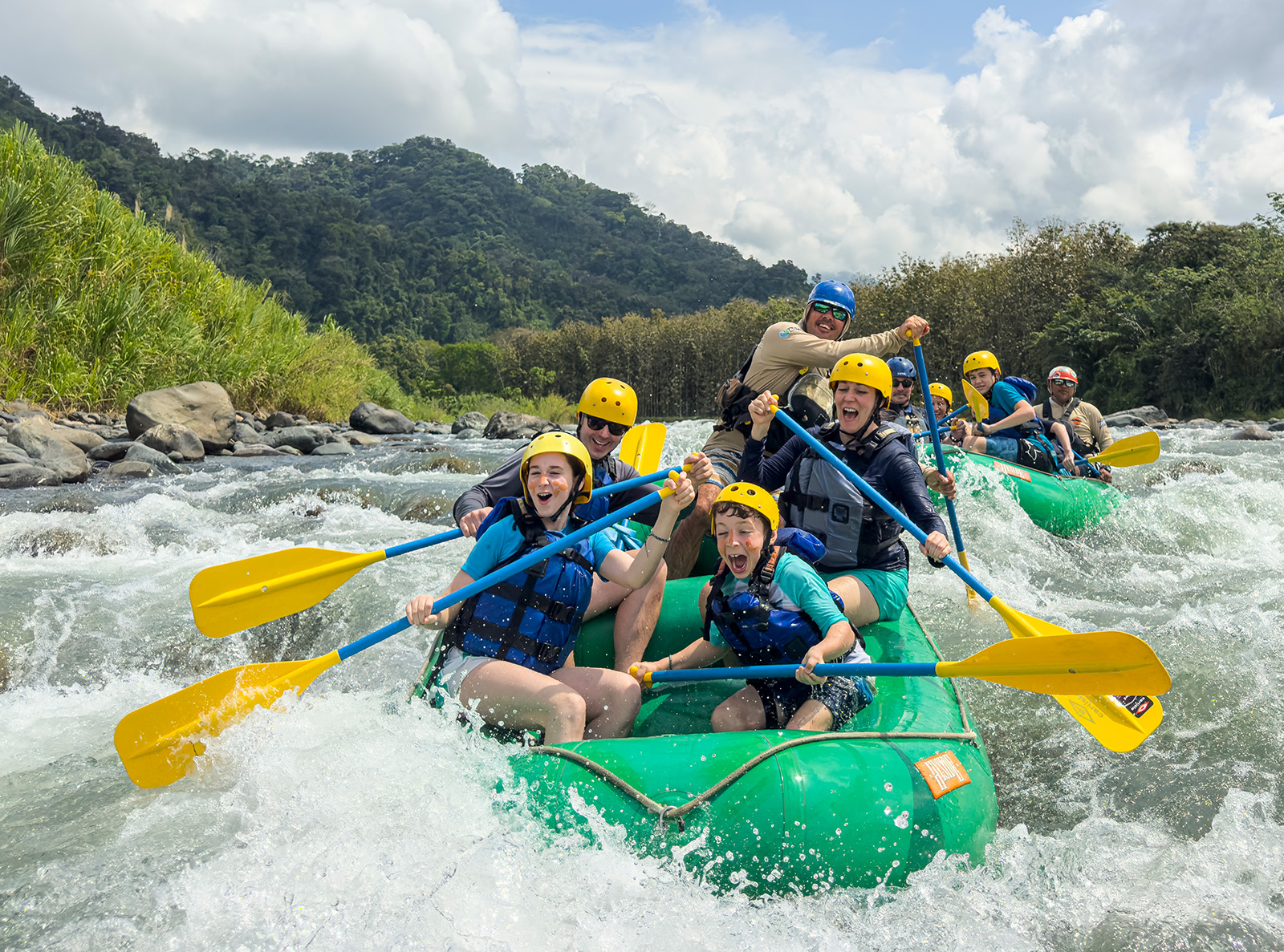 Two groups of families on green rafts, paddling in a river