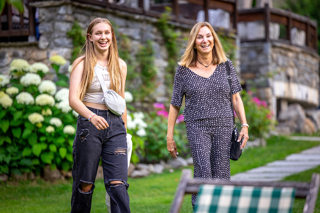 Two women standing and smiling on a grass field with flowers in the background