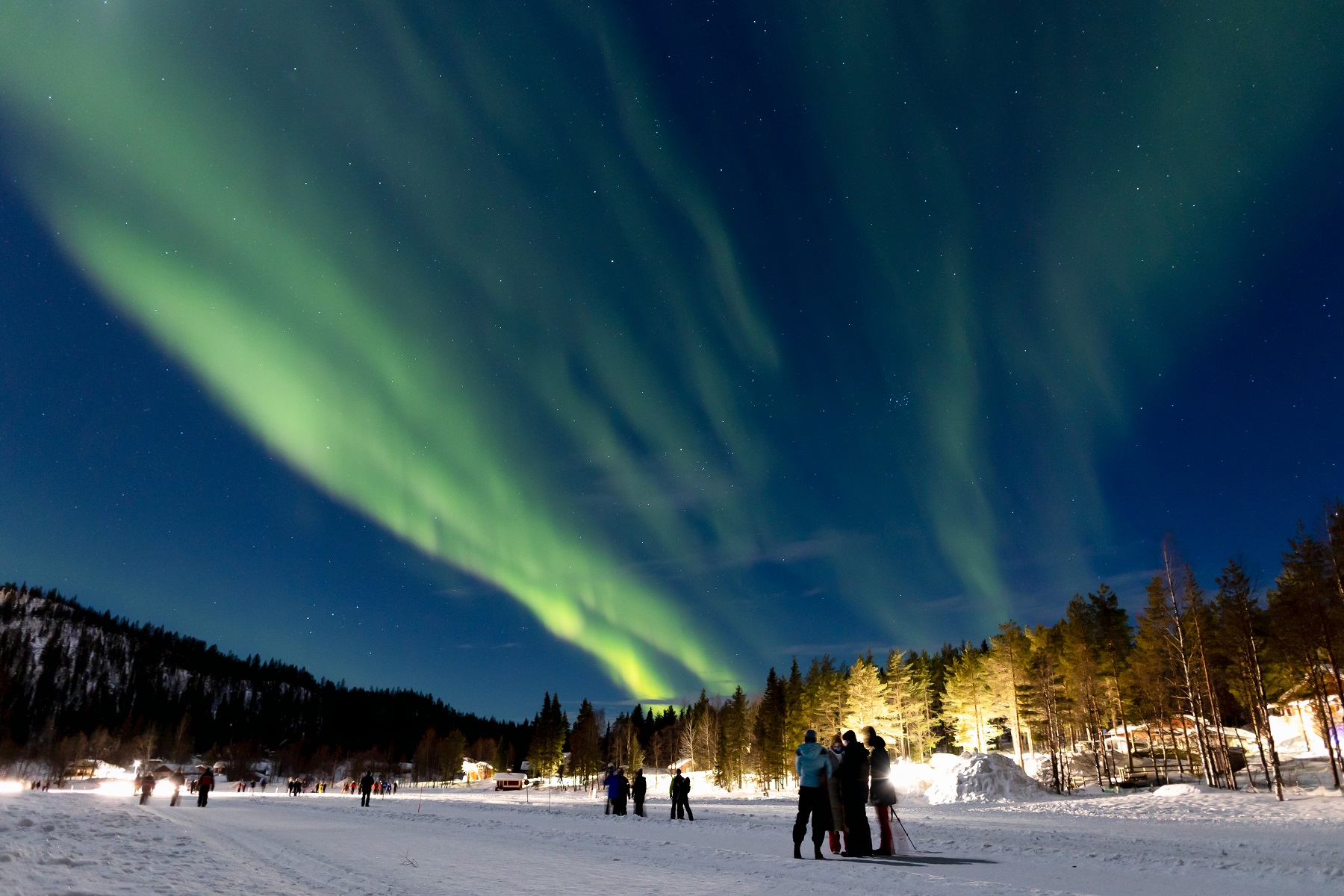 Group of people standing in the snow with an aurora in the sky
