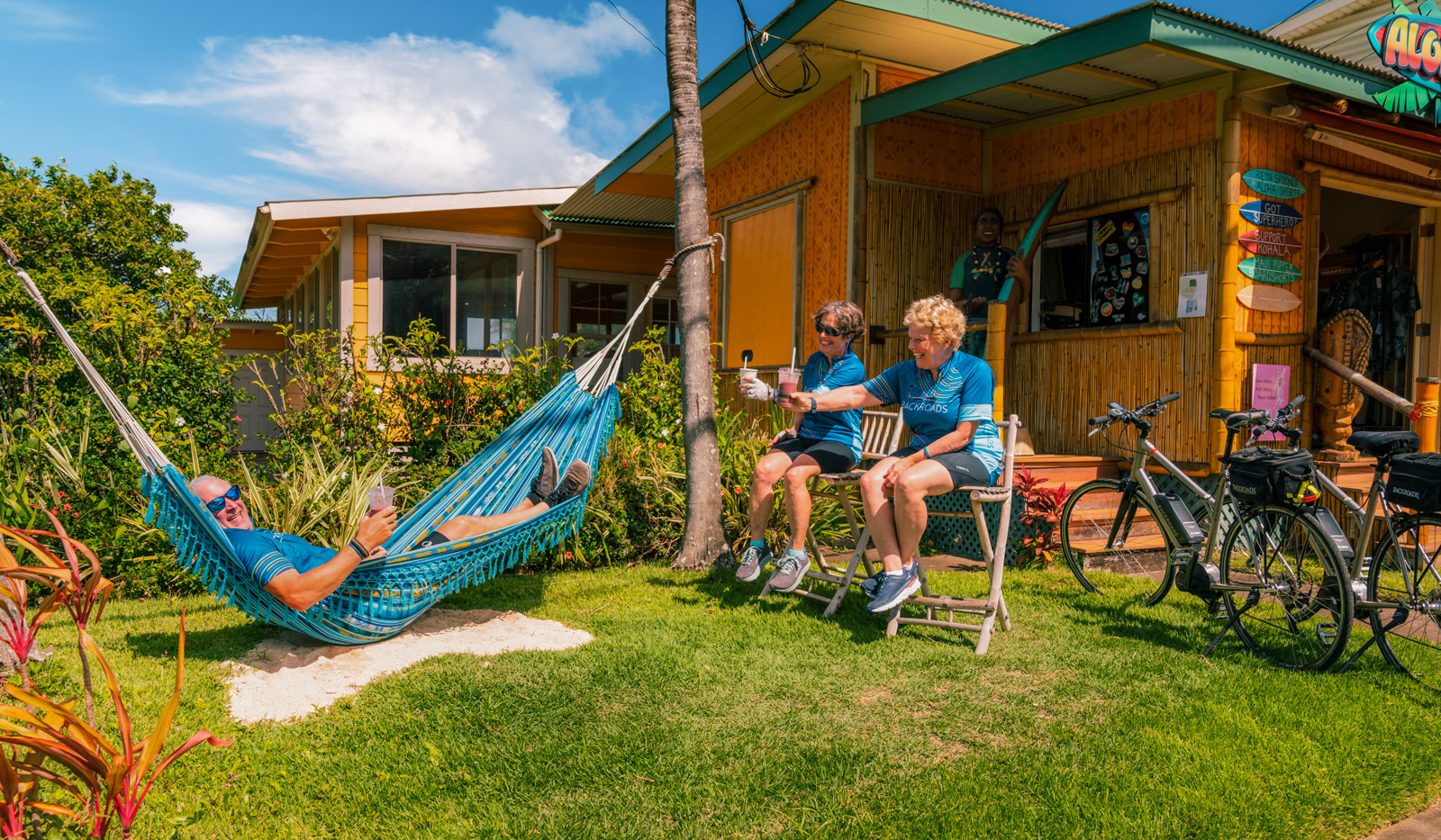 Man laying down on a hammock with two women sitting on wooden stools next to him