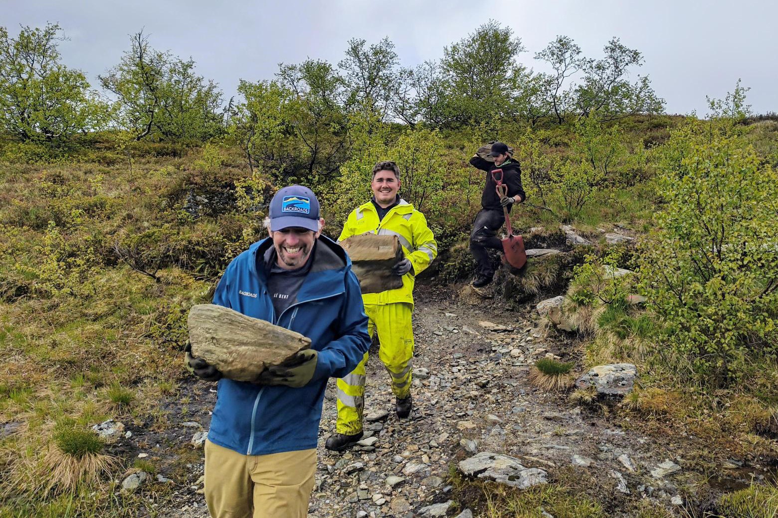 Two men smiling while carrying large rocks in the middle of a field