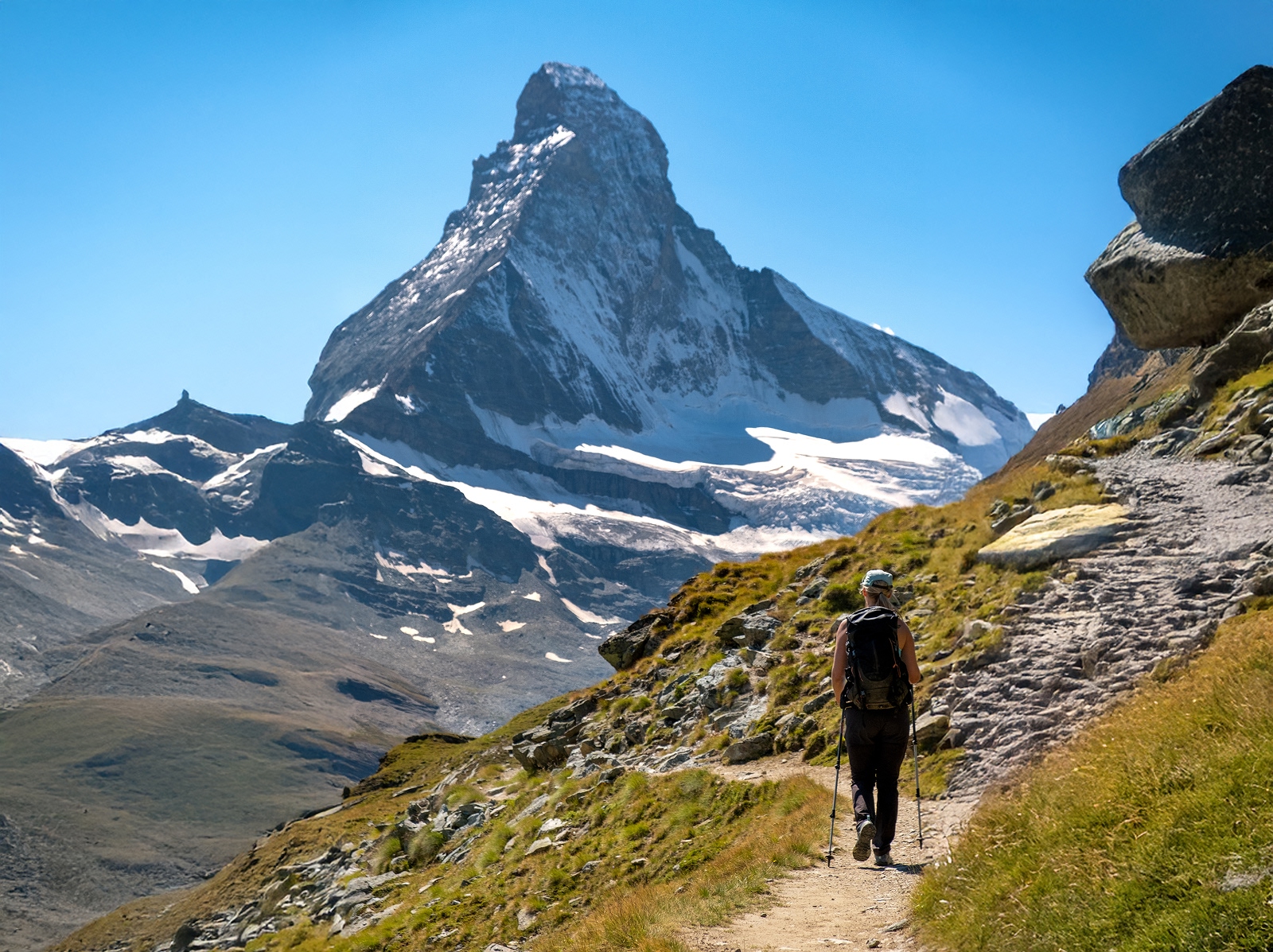 Woman using hiking poles, walking on a trail with tall mountains in front