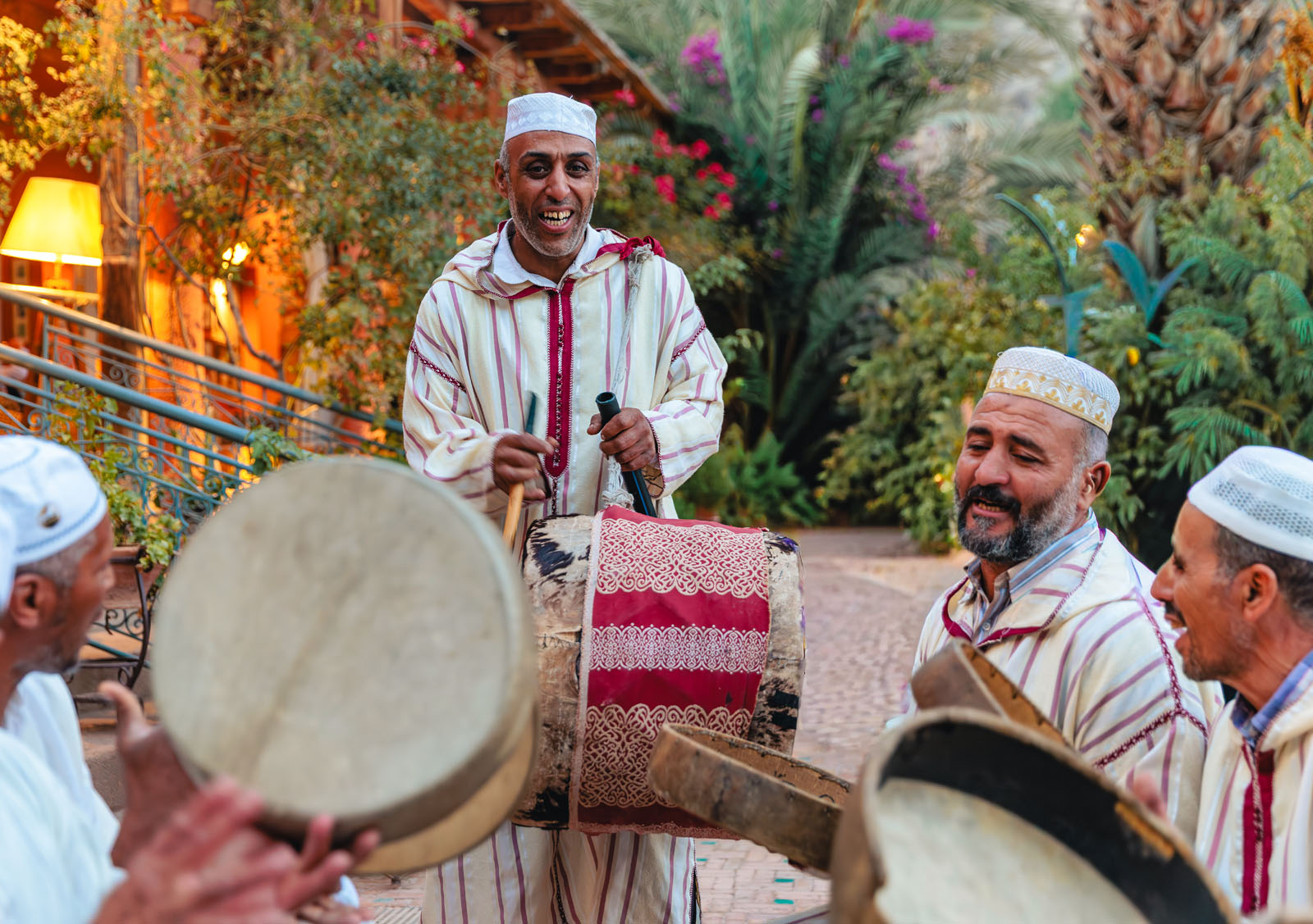Group of men wearing white, playing bongo-like instruments
