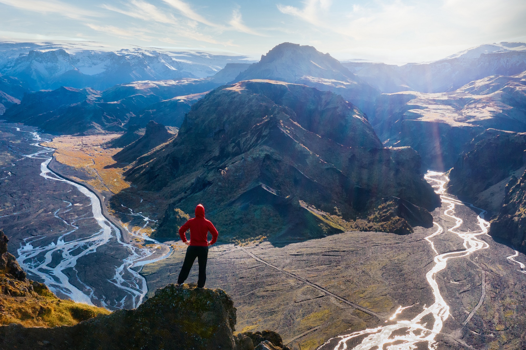 Person standing on a cliff looking out towards tall mountains