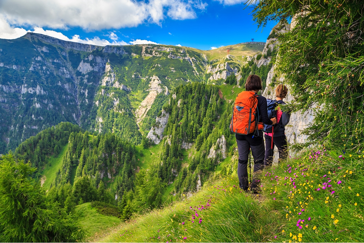 Two people walking on a grassy trail, with views of tall mountains