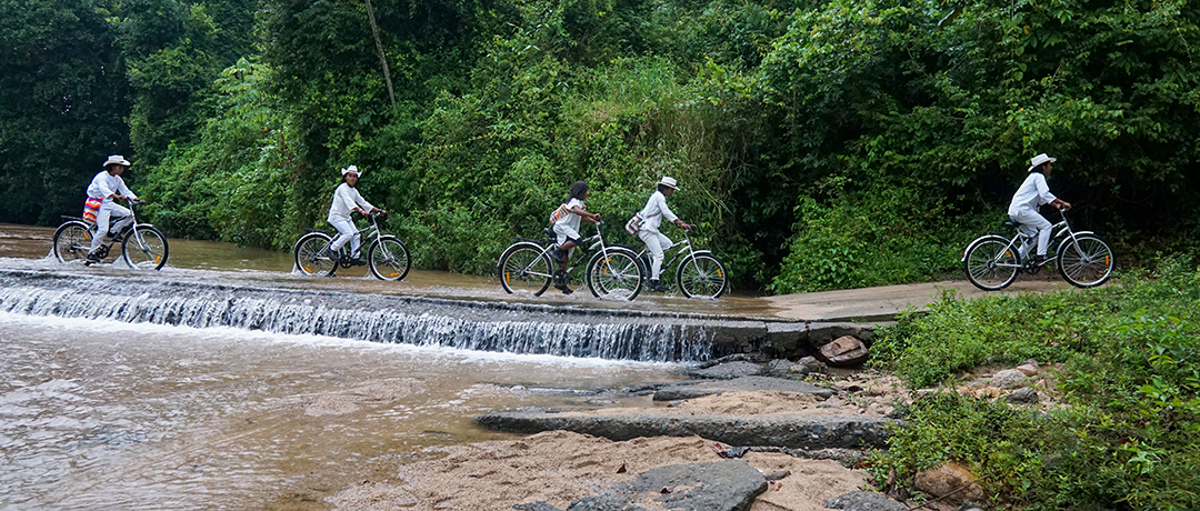 Group of people riding bikes on a road next to a small waterfall