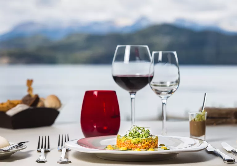 Plate of food with a wine glass and view of a lake in the background