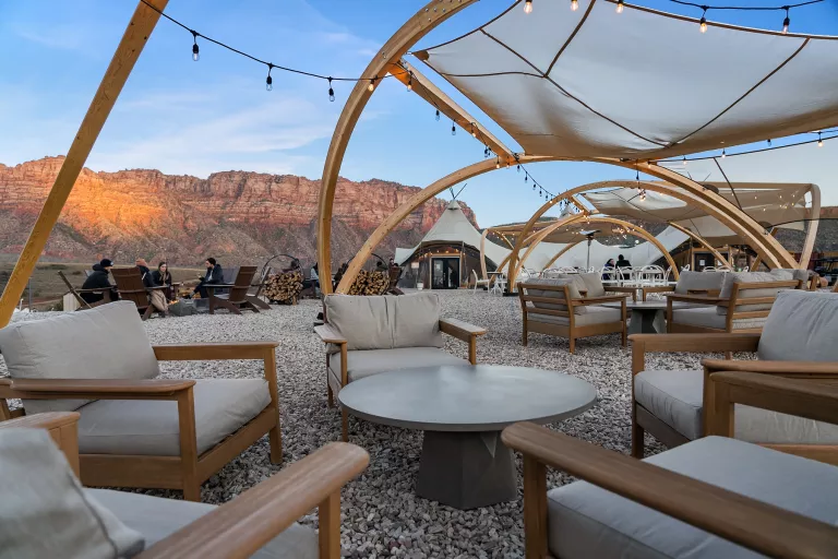 Gray, cushioned seats around a circular table on gravel, with large canyons in the background