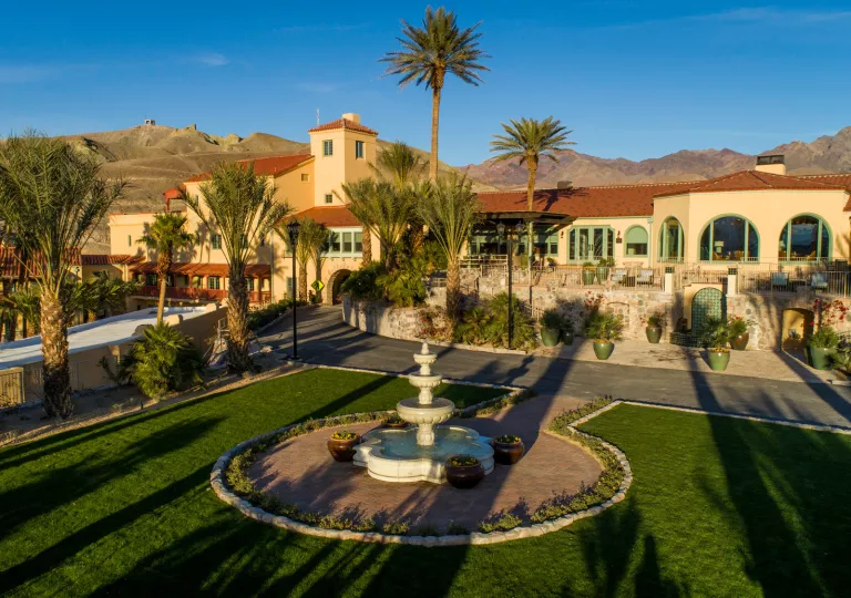 Exterior vide of tan and brown building, with a garden and circular fountain in front