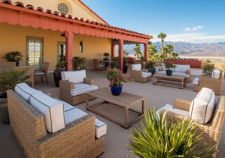 Outdoor patio with woven chairs and tables, with tall mountains in the distance