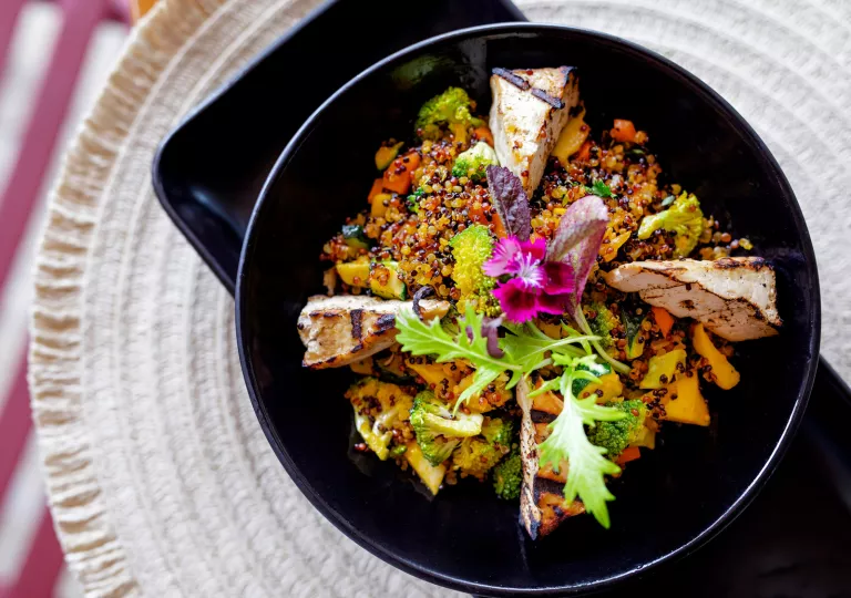 Black bowl filled with quinoa and grilled chicken and greens
