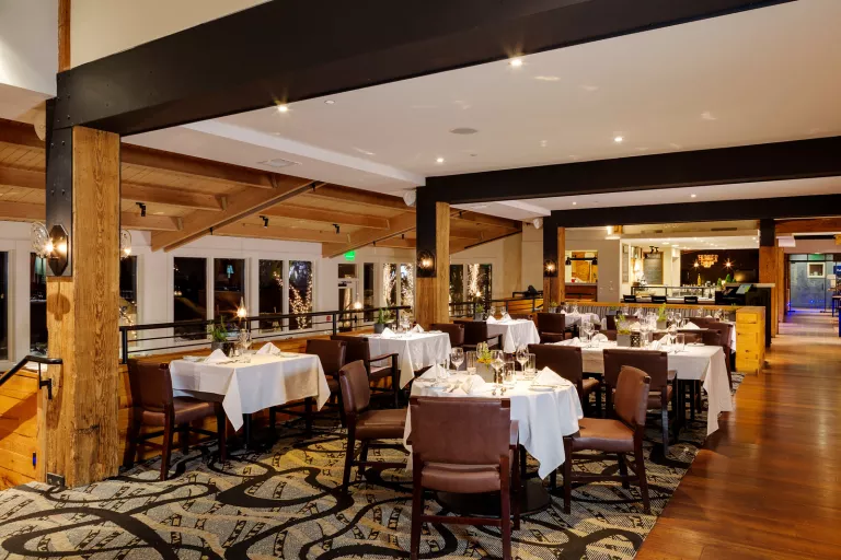 Indoor dining area with large black pillars, and leather chairs around white dining tables