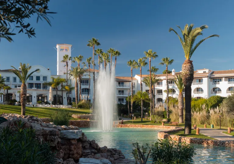 External view of a white hotel building with a large pond and a fountain in front