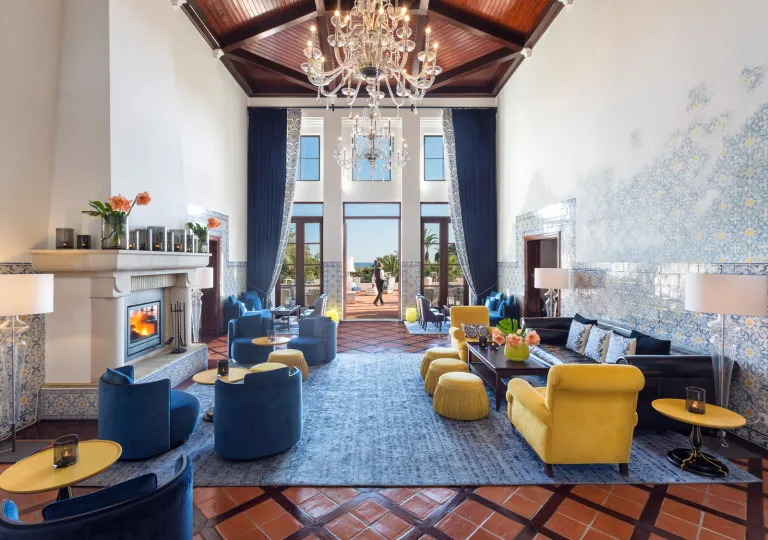 Indoor lounge with a large chandelier, and blue and yellow cushioned seats
