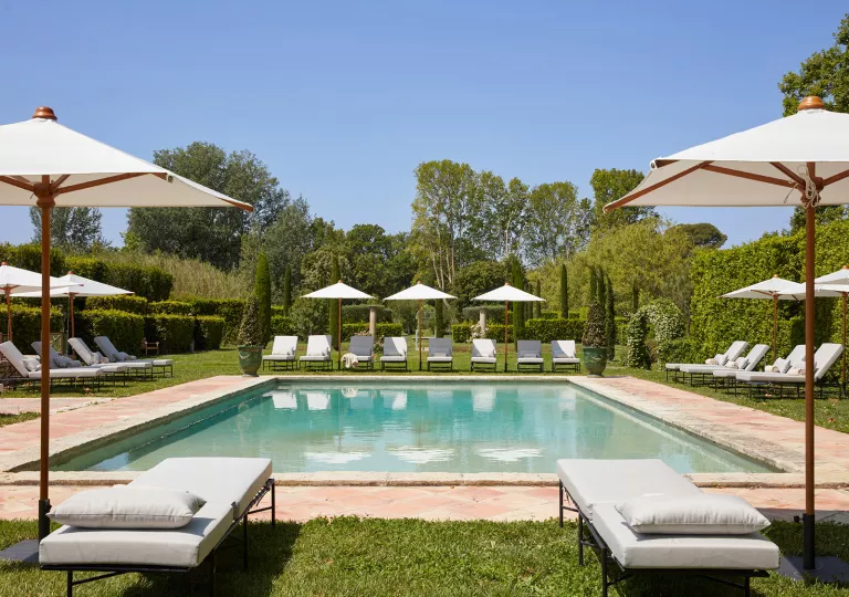 Outdoor pool with reclining pool chairs, surrounded by trees