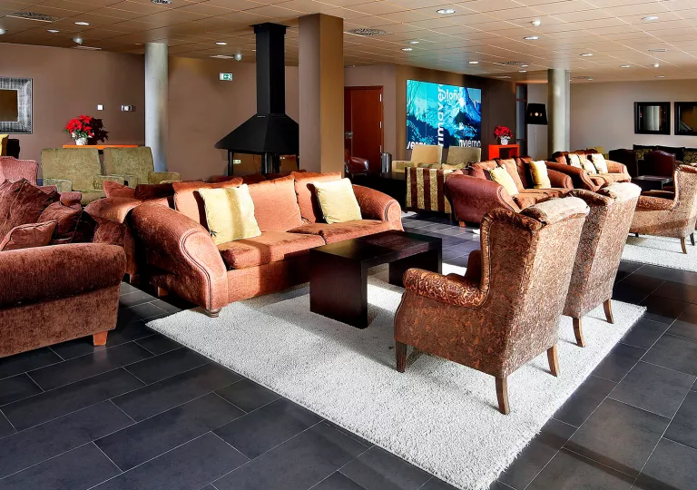 Lounge with red and brown, cushioned chairs with a metal fireplace in the center