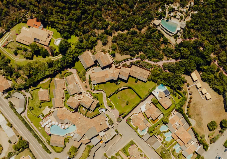 Sky view of tan colored buildings, surrounded by trees and minim outdoor pools