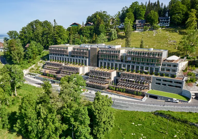 Exterior view of a long hotel complex, with large windows and tall trees
