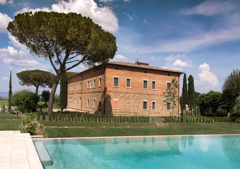Brick building with a large tree on the left and an outdoor pool in front