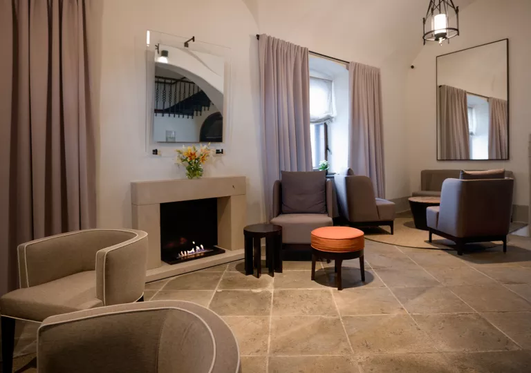 Indoor lounge with gray, cushioned chairs and a fireplace to the left