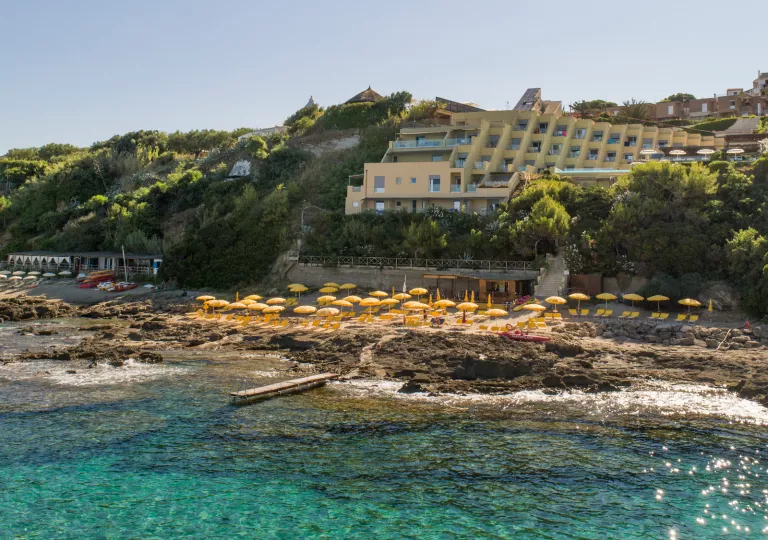 Ocean with a cluster of yellow umbrellas and chairs on a rock path, with a building in the background