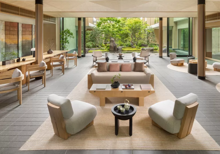 Outdoor patio with cushioned, white chairs and wooden tables, with a garden in the backrground