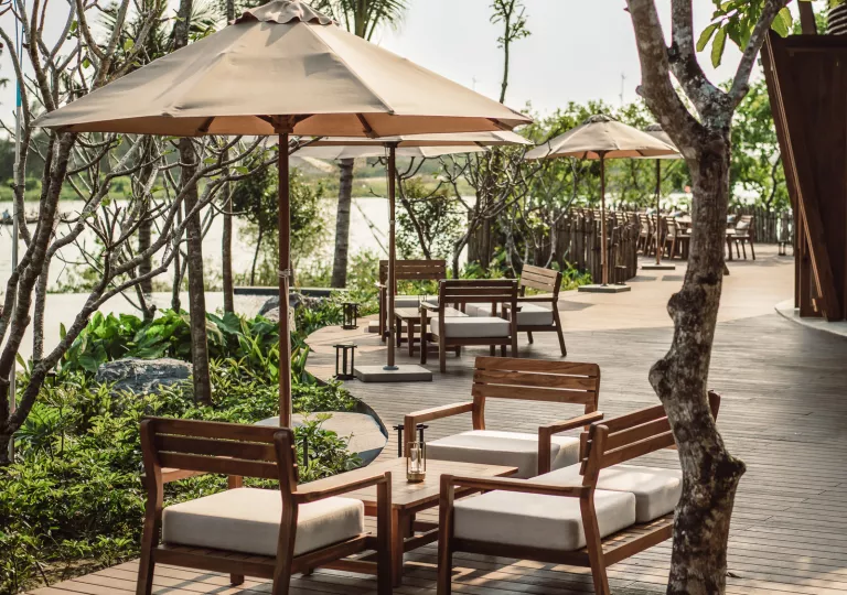 Outdoor patio on a wooden plank floor, with wooden chairs with gray cushioned and gray umbrellas