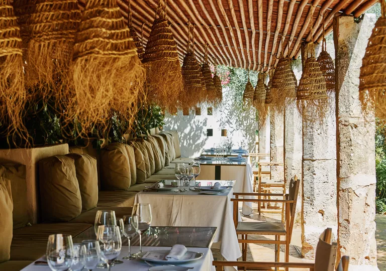 Outdoor patio with cushioned chairs and dining tables under a straw hut covering