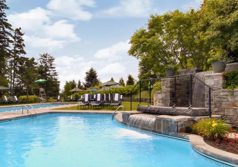 Outdoor pool with a small fountain to the right, and chairs in the background