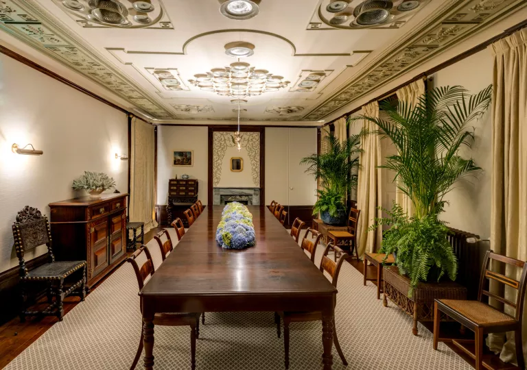 White room with large, wooden table with chairs surrounding it