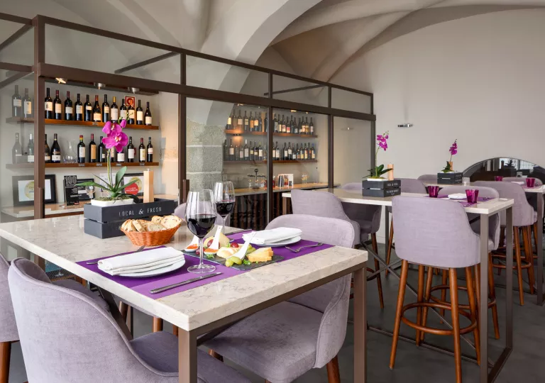 Restaurant dining hall with purple chairs and a clear shelf with bottles on wine