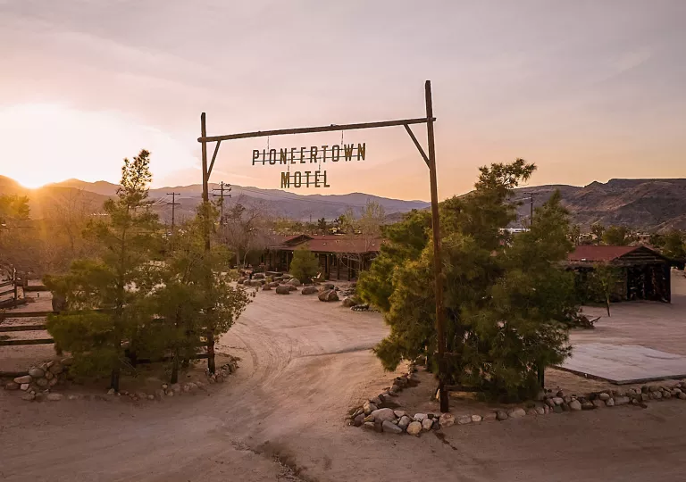 Dirt road leading to a large motel complex with a wooden sign saying "Pioneertown Motel"