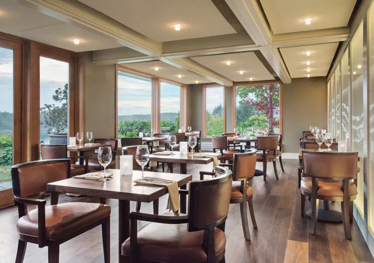 Dining hall with wooden tables and leather chairs, with wine glasses on each table