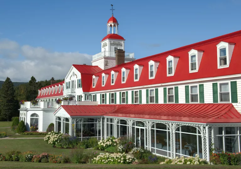 Exterior view of long red and white hotel building with bushes and a garden in front