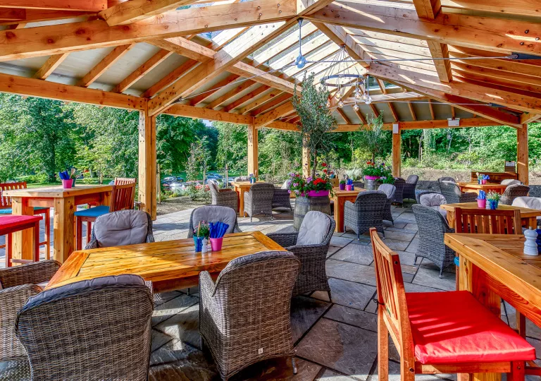 Outdoor patio and garden with cushioned, gray chairs around wooden tables