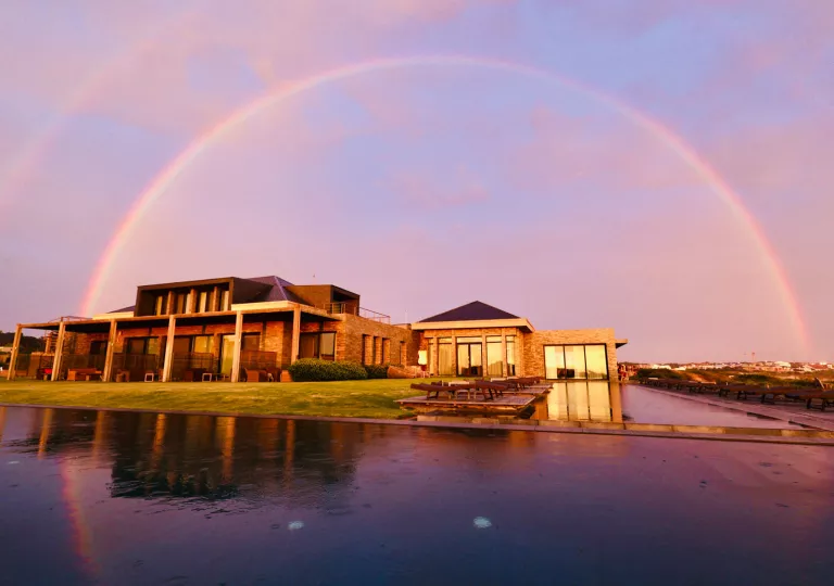 Hotel complex with a large pool in front, with a rainbow in the sky