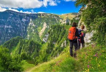 Two people walking on a grassy trail, with views of tall mountains